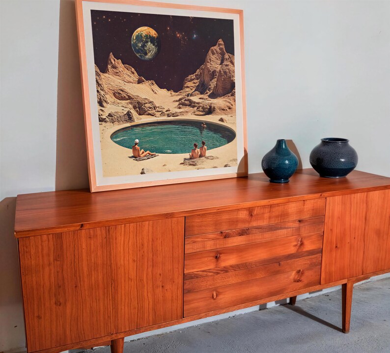 a wooden cabinet with a framed picture of a desert landscape with a pool of water in the center. The cabinet has two vases on top of it.