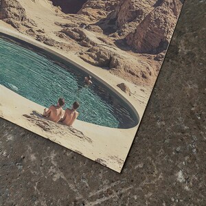 Two people sitting on a rock near a pool, with a desert landscape in the background.
