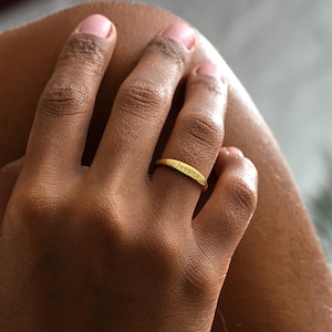 May include: A gold ring engraved with the name "Jessica". The ring is worn on a finger, with the hand and arm visible. The ring has a simple, elegant design. The ring is likely made of gold.