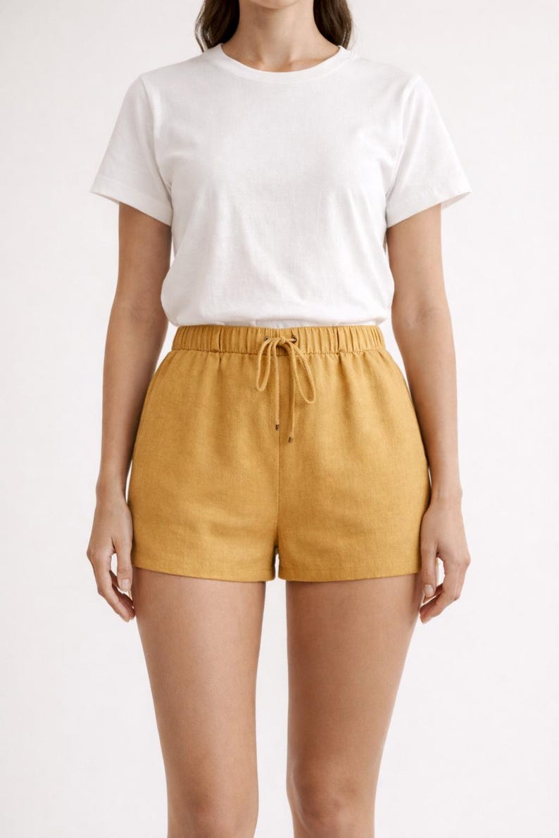 May include: A white crew neck t-shirt paired with mustard yellow shorts. The shorts have an elastic waistband with a drawstring. The outfit is casual and suitable for warm weather.