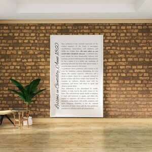 May include: A framed print with the text "Lessons in Gentility, Anno 1860" against a brick wall. The print features a lengthy passage of text in a serif font. A small potted plant and side table are in the foreground.