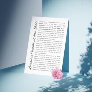 May include: A white paper with the text "Lessons in Gentility, Anno 1860" and a passage about true politeness, with a pink flower in the lower right corner. The paper is angled against a blue surface.