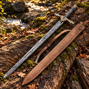 May include: A Damascus steel sword with a wavy patterned blade and an ornate gold-toned crossguard featuring a central dark stone. The handle is wrapped in dark textured material with a crown-shaped pommel, accompanied by a tan leather scabbard.