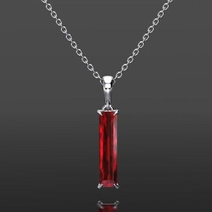 Puede incluir: Un collar de plata con un colgante rectangular de color rojo intenso. El colgante cuelga de una delicada cadena, creando un diseño simple pero elegante. La piedra preciosa es de un color rojo vibrante y saturado.