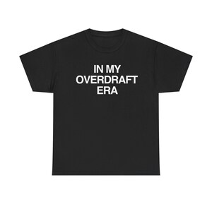 Könnte beinhalten: Schwarzes T-Shirt mit dem weißen Text "IN MY OVERDRAFT ERA". Das T-Shirt hat einen Rundhalsausschnitt und kurze Ärmel. Der Text ist mittig auf der Vorderseite des T-Shirts platziert.