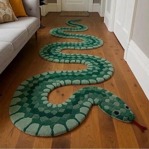 Può includere: Un lungo tappeto a forma di serpente con un motivo ripetuto di squame verde scuro e verde chiaro. Il tappeto presenta una testa arrotondata con due occhi neri e una lingua rossa biforcuta che sporge, disteso sul pavimento.