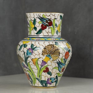 May include: A decorative ceramic vase with a cream-colored background and intricate floral designs in various colors. The vase features a textured surface and gold accents, showcasing a traditional aesthetic. The vase is approximately 10 inches tall.