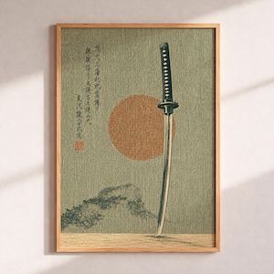 May include: Framed print depicting a katana sword with a black handle and silver blade. The artwork includes a large orange sun and Japanese text on a textured, muted green background. The wooden frame adds a classic touch.