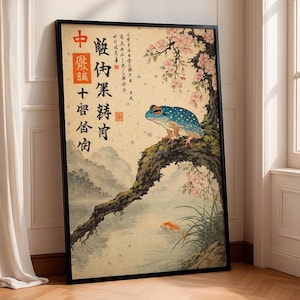Puede incluir: Impresión artística enmarcada que presenta una rana azul moteada posada en una rama de árbol, con flores de cerezo y peces koi en un estanque. La obra de arte tiene texto japonés y una estética tradicional.