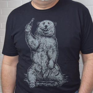 Puede incluir: Una camiseta negra con un gráfico de un oso sosteniendo una botella de cerveza. El oso está sentado en una roca y tiene una expresión relajada.
