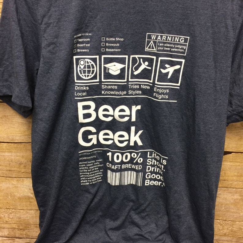 Puede incluir: Una camiseta azul oscuro con un dise&ntilde;o gr&aacute;fico blanco que dice "Beer Geek" e incluye una lista de verificaci&oacute;n de actividades relacionadas con la cerveza. El gr&aacute;fico tambi&eacute;n incluye el texto "100% Craft Brewed" y "Life is Short. Drink Good Beer."