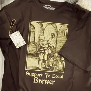 May include: A brown t-shirt with a vintage-style illustration of a brewer holding a mug, with the text "Support Ye Local Brewer." The shirt has a tag that says "Deck Halls."