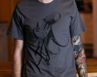 May include: A dark gray t-shirt with a black and white illustration of an octopus holding a bottle of beer.