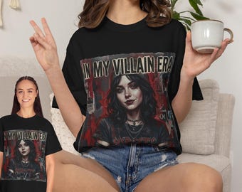 Puede incluir: Una camiseta negra con un estampado gráfico de una persona de pelo oscuro con una sonrisa burlona, collares superpuestos y el texto "IN MY VILLAIN ERA" en una fuente negrita y desgastada. El diseño incluye acentos rojos y oscuros con textura.