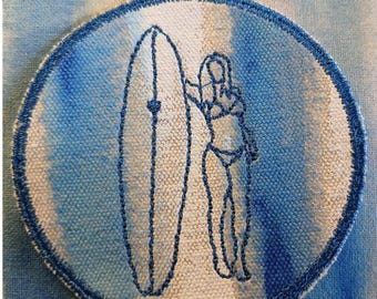 Puede incluir: Parche bordado con un diseño de surfista y tabla de surf. El contorno azul está sobre un fondo blanco, dentro de un círculo azul y blanco estilo acuarela. El parche tiene un borde cosido azul.