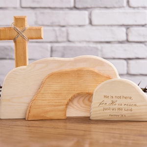 Könnte beinhalten: Osterszene aus Holz mit einem Kreuz, einem Grab und einem Zitat aus Matthäus 28,6. Das Kreuz ist mit Bindfaden gebunden. Das Grab besteht aus geschichtetem Holz. Der Text lautet: „Er ist nicht hier, denn er ist auferstanden, wie er gesagt hat.“