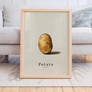 Puede incluir: Un póster enmarcado con una ilustración realista de una patata. La patata es de color marrón claro con manchas más oscuras, sobre un fondo neutro. La palabra "Potato" está impresa debajo de la imagen.