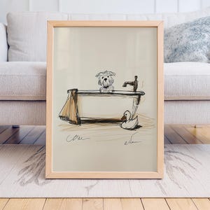 Op de afbeelding: Een ingelijste schets toont een hond in een badkuip met een kraan en een badeend. Het kunstwerk gebruikt bruine en zwarte lijnen op een beige achtergrond. Een bruine handdoek hangt aan de zijkant van de kuip. De lijst is van licht hout.