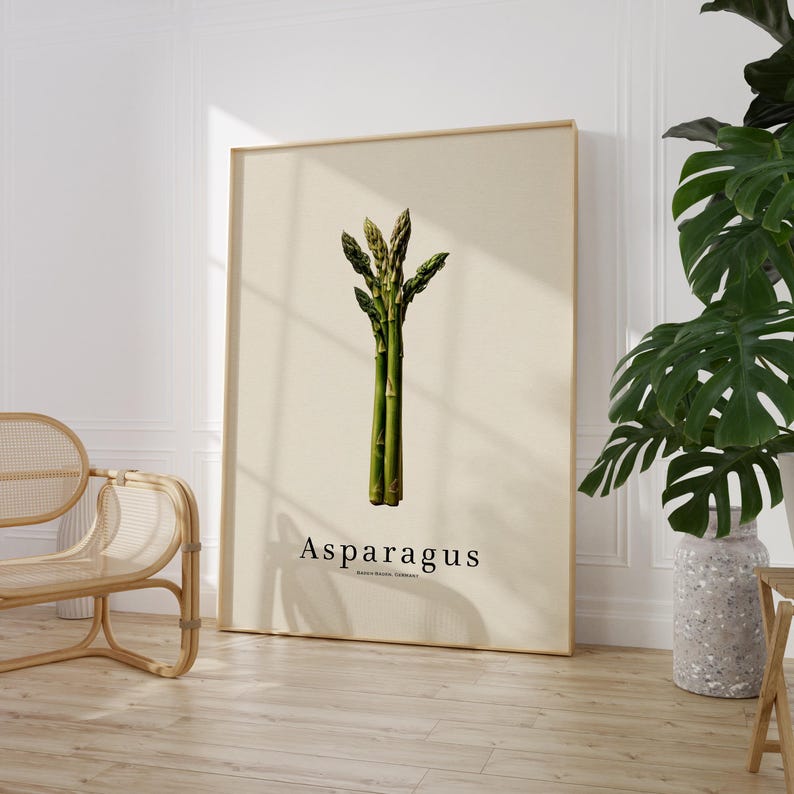 May include: A framed botanical print featuring a detailed illustration of asparagus. The artwork showcases a bundle of green asparagus stalks against a beige background. The word "Asparagus" is printed in a simple font below the illustration.