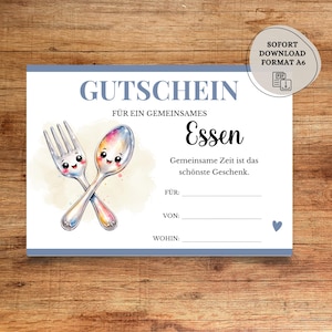 Pode incluir: Um vale-presente branco com uma borda azul e texto em alemão. Apresenta um garfo e uma colher de desenho animado com rostos sorridentes. O texto inclui "GUTSCHEIN" e "Essen". Um pequeno ícone de coração na parte inferior.