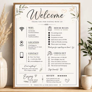 May include: A framed white sign with black text and botanical illustrations. The sign features sections for WiFi, house rules, location, contact information, check-out instructions, and a review request, all written in a clear, sans-serif font.