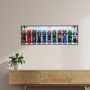 Peut inclure: Une affiche encadrée présentant dix voitures de course de Formule 1 colorées. Chaque voiture arbore une couleur et un design différents, sur fond blanc avec un cadre noir. L'affiche est au-dessus d'un meuble en bois.