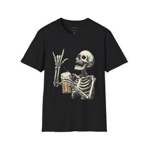 Könnte beinhalten: Schwarzes T-Shirt mit einer detaillierten Illustration eines Skeletts, das einen Bierkrug hält und eine Rock'n'Roll-Handbewegung macht. Das Skelett ist in einem Vintage-Stil dargestellt, mit dem Bierkrug gefüllt mit einem schaumigen, goldenen Getränk.