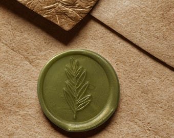 May include: A close-up of a green wax seal with a leaf design, resting on a brown paper envelope. The seal has a metallic sheen. A textured, gold-colored paper is in the background.