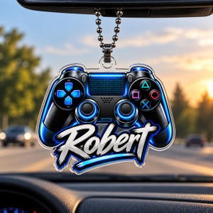 May include: A clear acrylic car hanging ornament shaped like a video game controller with blue neon-style accents and the name Robert printed in a bold white script font across the bottom, suspended by a silver-toned metal ball chain.