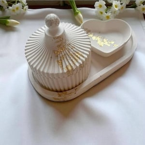 Puede incluir: Una caja de baratijas blanca con tapa, un plato en forma de corazón y una bandeja, decorados con detalles de pan de oro. La caja tiene un diseño acanalado y un pomo esférico. La bandeja es curva.