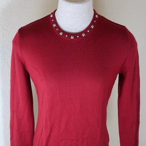 May include: A long-sleeved, red sweater with a silver studded neckline and cuffs.