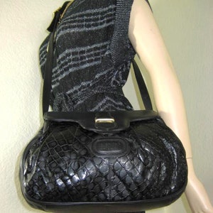 May include: A black leather shoulder bag with a crocodile-embossed pattern. The bag has a flap closure with a gold-tone buckle and a long adjustable strap.