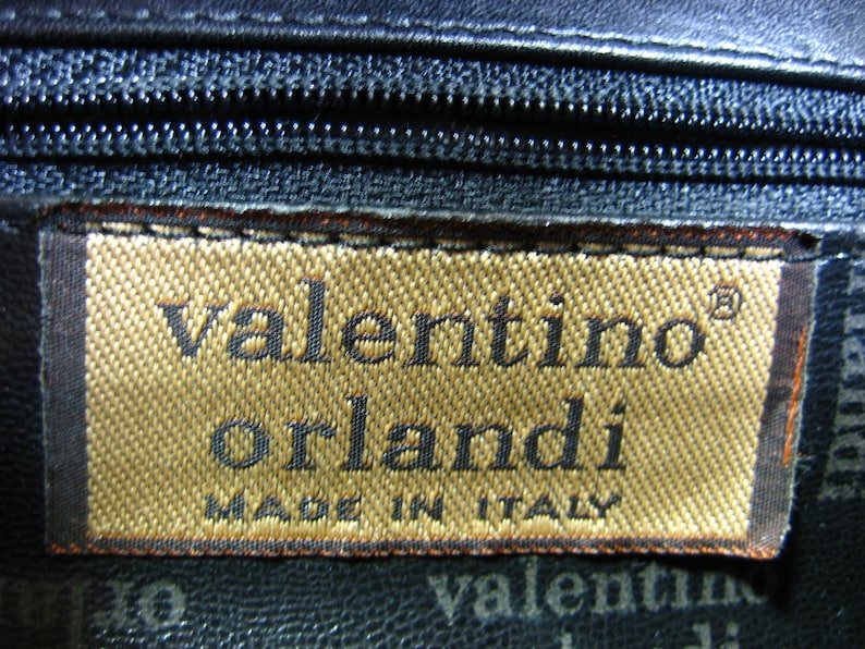 May include: A brown leather purse with a gold label that reads "valentino orlandi made in italy".