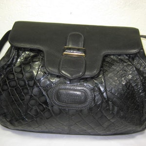 May include: A black leather handbag with a crocodile-embossed pattern and a gold-toned clasp. The bag has a single strap and a flap closure.