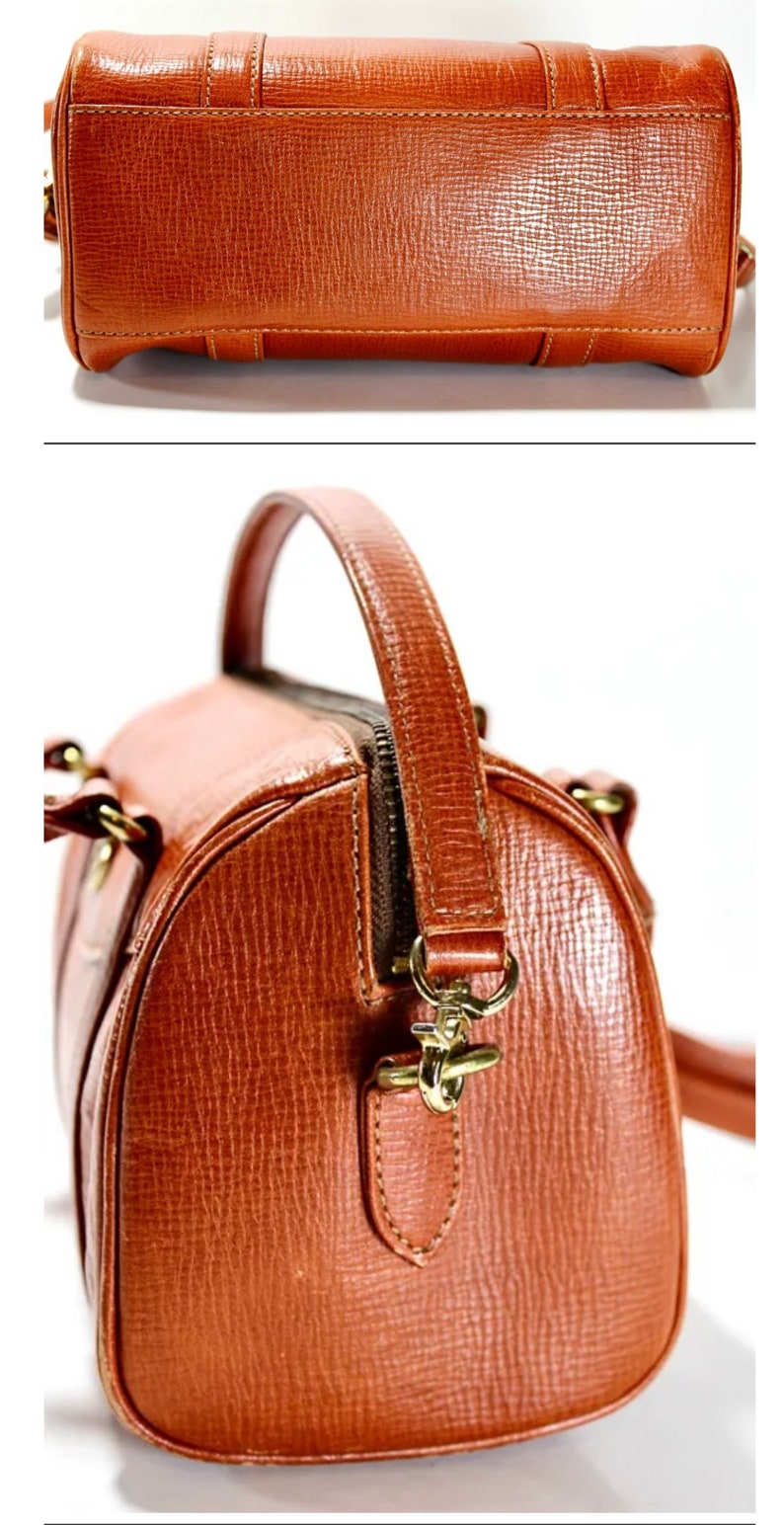 Puede incluir: Un bolso de cuero marr&oacute;n con una hebilla dorada y un asa superior. El bolso tiene un acabado texturizado y una cremallera.