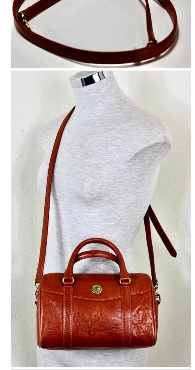 Puede incluir: Un bolso de mano de cuero marr&oacute;n con una hebilla dorada y una correa larga ajustable. El bolso tiene un asa superior y una correa para el hombro.