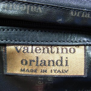 May include: Close-up of a black leather bag with a brown label that reads "valentino orlandi made in italy".