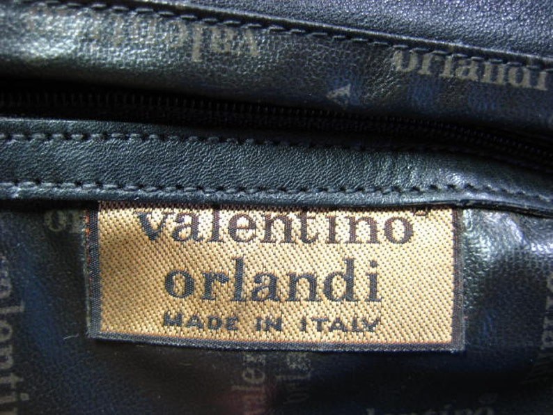 May include: Close-up of a black leather bag with a brown label that reads "valentino orlandi made in italy".