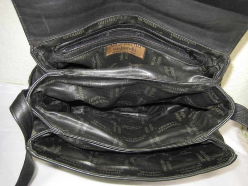 May include: Black leather handbag with multiple compartments and a zipper closure. The bag has the text "Valentino Orlandi" printed on the inside.