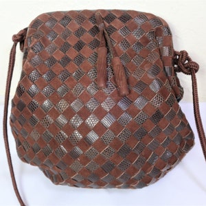 May include: A brown leather handbag with a woven pattern and a drawstring closure. The bag has a long strap and two tassels.