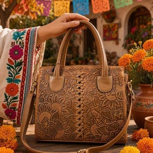 May include: A tan leather handbag featuring an intricate embossed floral pattern across the front and a central vertical braided leather detail. The bag includes two top handles and a detachable, adjustable shoulder strap with metal hardware.