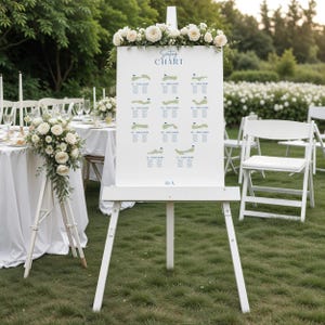 Op de afbeelding: Een witte ezel toont een plattegrond met illustraties van golfbanen. De kaart is versierd met bloemstukken en de tekst "Seating Chart". De scène speelt zich buiten af met tafels, stoelen en groen, wat duidt op een bruiloft of evenement.