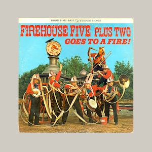 May include: A vintage record album cover featuring a red fire engine with a group of firefighters playing musical instruments. The album title is "Firehouse Five Plus Two Goes To A Fire!"