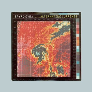 May include: A vintage album cover with a red, orange, and yellow color scheme. The cover features a graphic of a weather map with a hurricane in the center. The album title "SPYRO GYRA... ALTERNATING CURRENTS" is printed in black at the top of the cover.