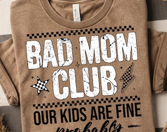Può includere: Maglietta color beige con la scritta "BAD MOM CLUB" in lettere bianche usurate. Sotto, il testo "OUR KIDS ARE FINE - probably" è scritto in nero. Il design include una stella a scacchi e un fulmine.