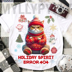 May include: White t-shirt with a grumpy cat in a red and white festive outfit. The shirt displays "HOLIDAY SPIRIT ERROR 404" and "HAPPY MEOW YEAR". Christmas-themed illustrations of a snowman, baubles, and snowflakes surround the cat.