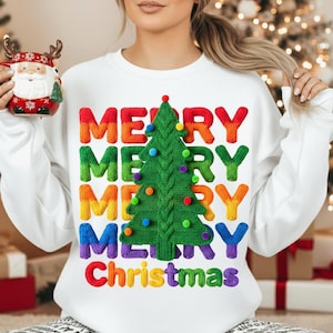 Puede incluir: Sudadera blanca con un diseño colorido de "Merry Christmas". El diseño presenta las palabras "Merry Christmas" en colores del arcoíris, con un árbol de Navidad verde en el centro. Un artículo festivo de vacaciones.