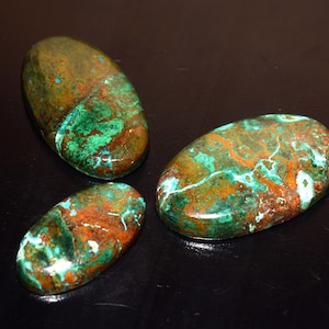 May include: Three polished, oval-shaped stones with a mix of colors. The stones have a base of brown and green, with streaks of turquoise and white. The stones are smooth and appear to be natural gemstones.