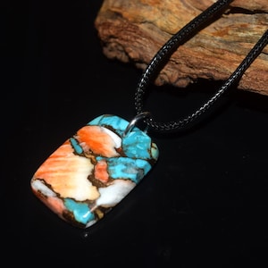 May include: A rectangular pendant featuring a mosaic of turquoise, orange, and white stone segments separated by dark matrix veins. The pendant is suspended from a thin black cord, creating a necklace with a smooth, polished surface finish.