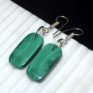 May include: A pair of green malachite earrings. Each earring features a rectangular, polished malachite stone with a unique pattern of light and dark green swirls. The stones are suspended from silver-colored ear wires.